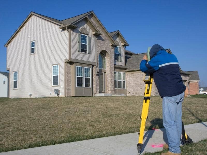 Land surveyor using a total station for land surveying on a residential property