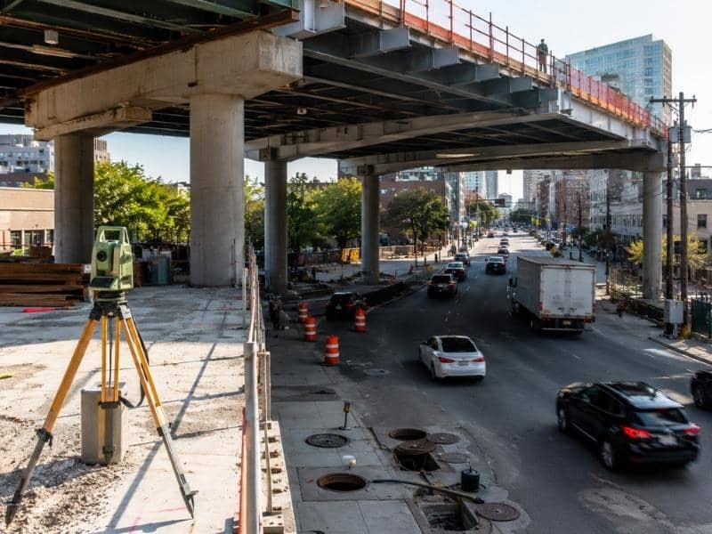 Elevated structure under construction above an active roadway with surveyed columns positioned around existing utilities